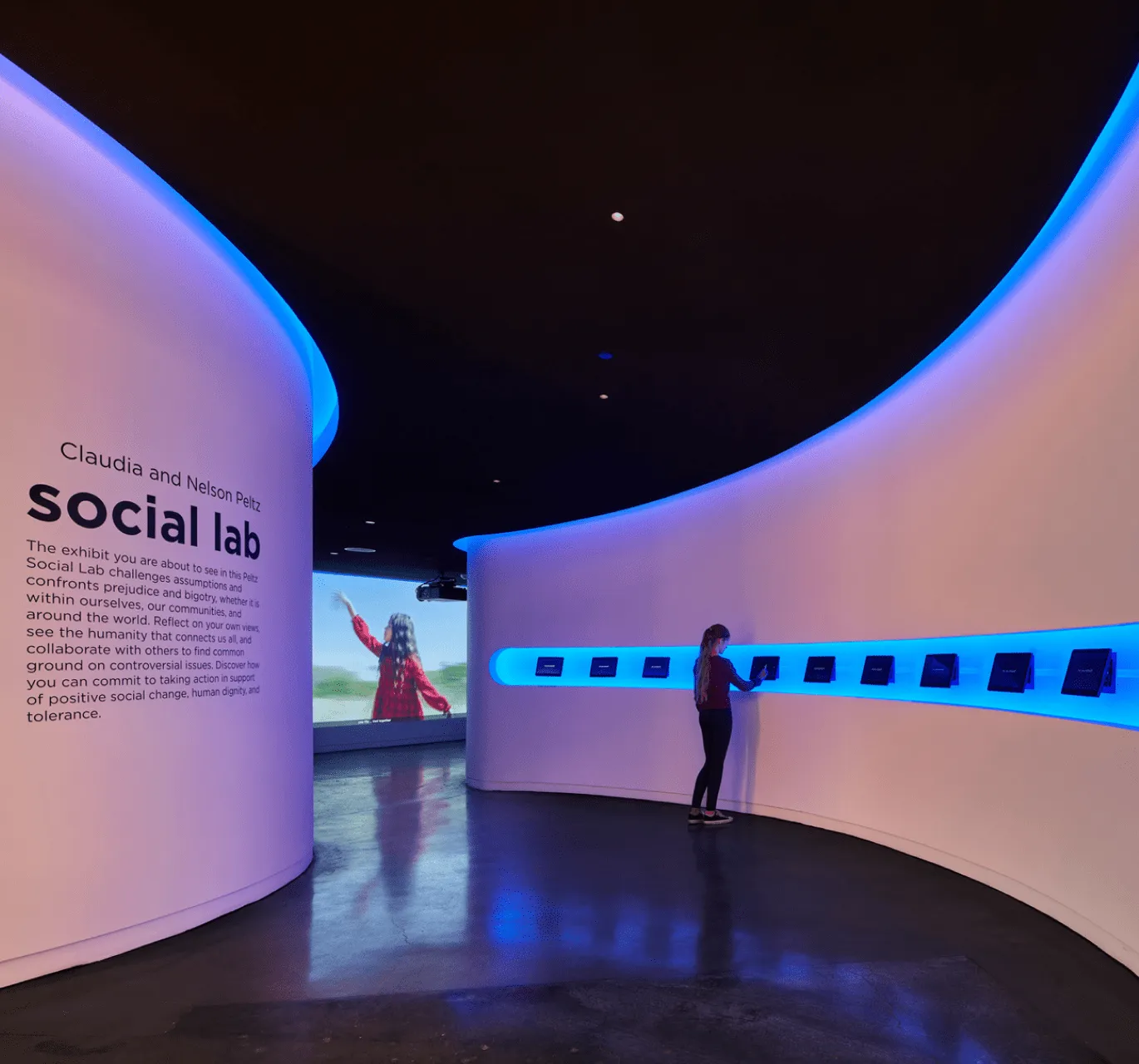 A visitor stands in the museum passageway while interacting with a small touchscreen.