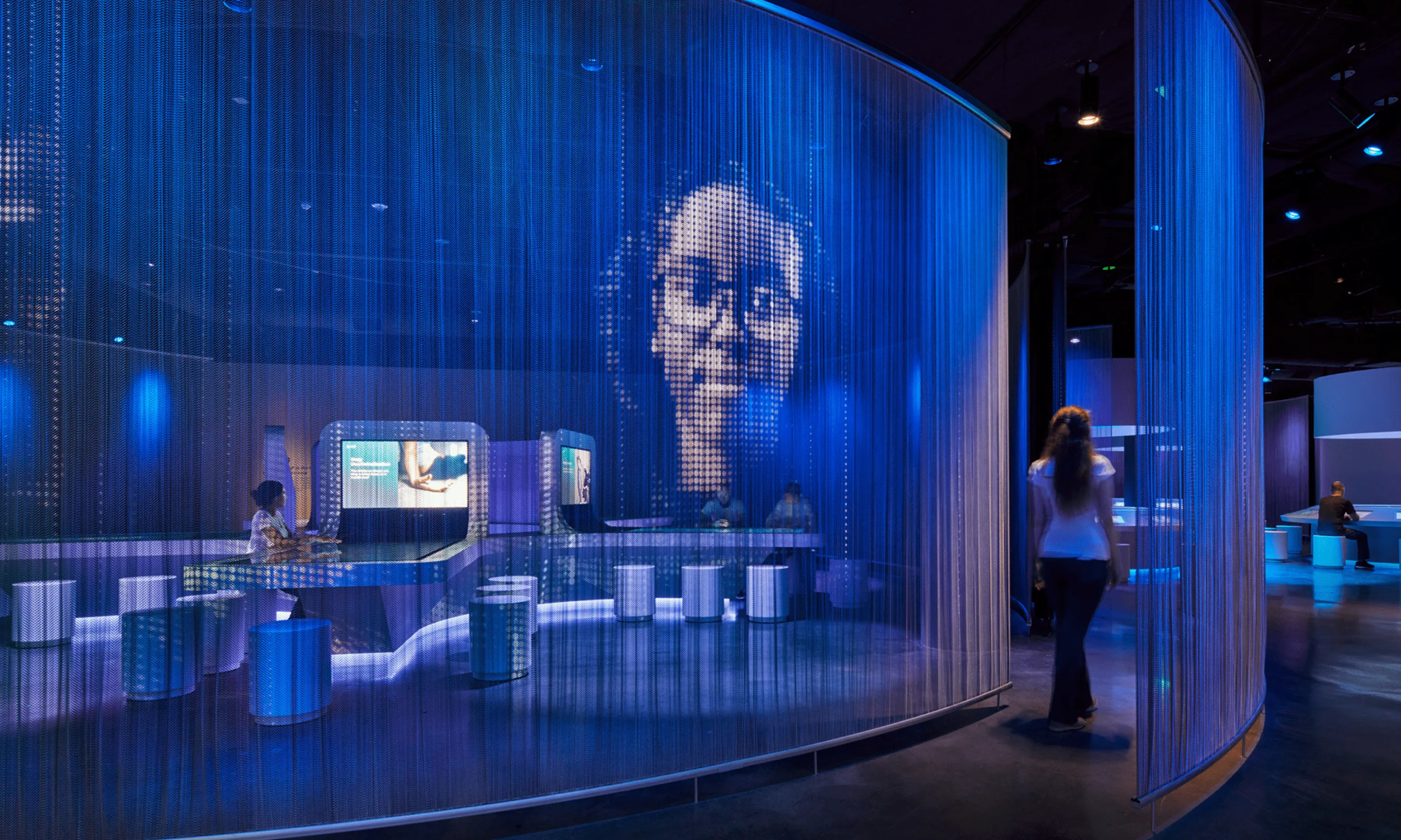 The mesh projection displays a person's face in the passageway, guiding visitors through to different sections of the museum's social lab.