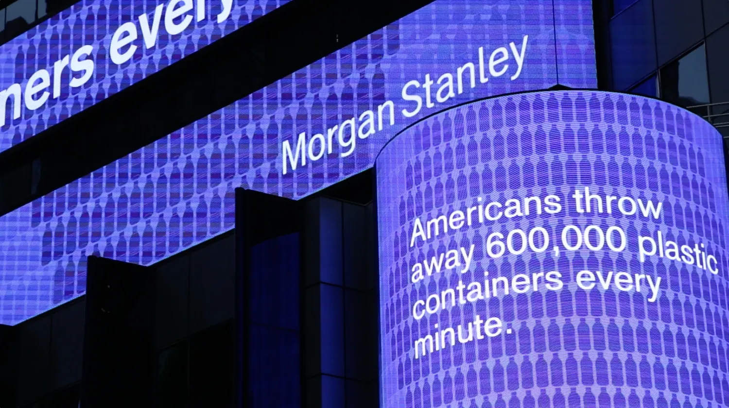 Digital signage at a street corner reads, "Americans throw away 600,000 plastic containers every minute."