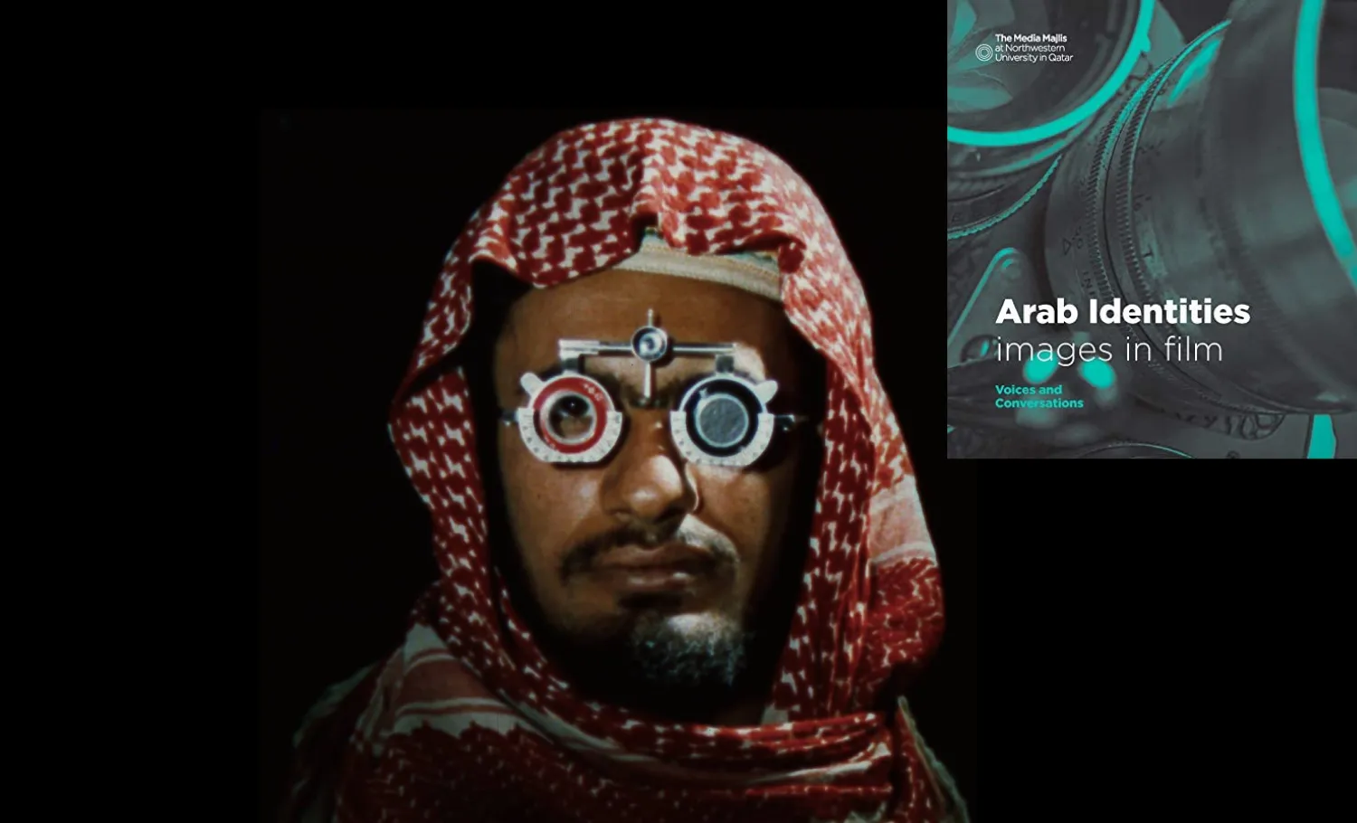 A man wearing kaffiyeh and phoropter glasses stand in front of a projection screen.