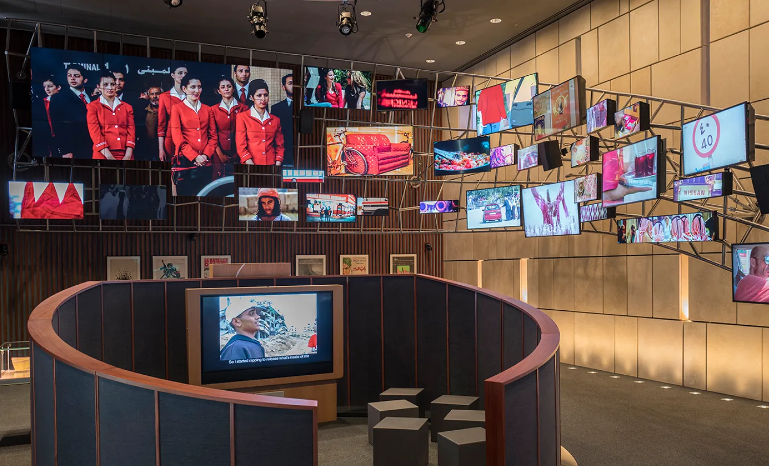 Different sized screens are hung across the exhibition room, with seatings shown in the foreground.