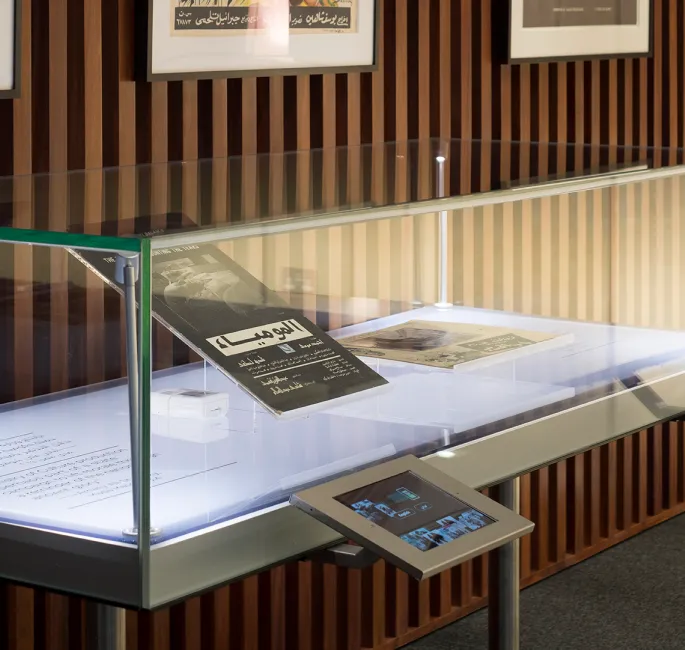 Digital kiosk sits in front of an artifact case containing archival items of Arab film history.