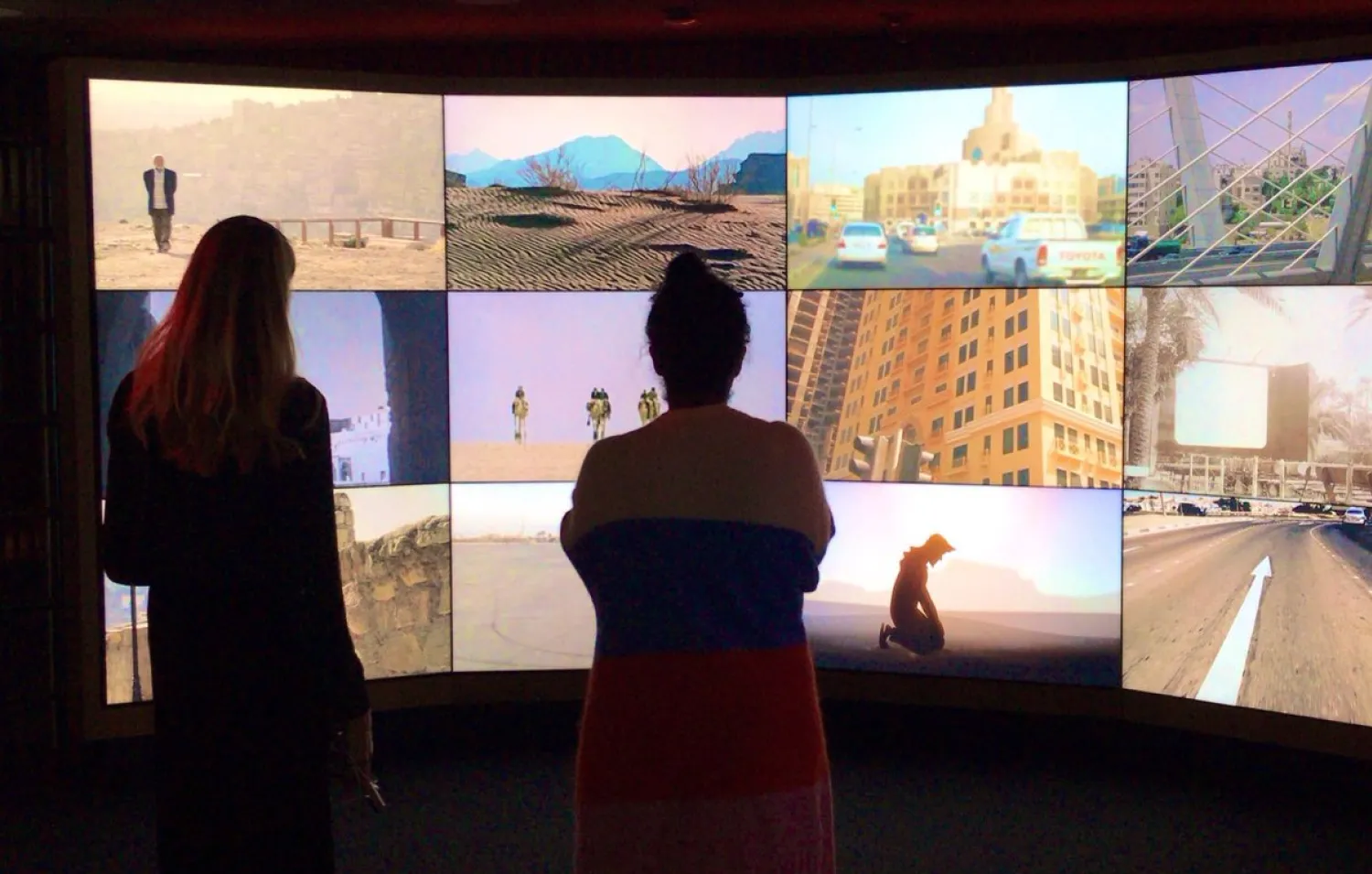 Visitors stand to watch a montage of films shown across several screens.