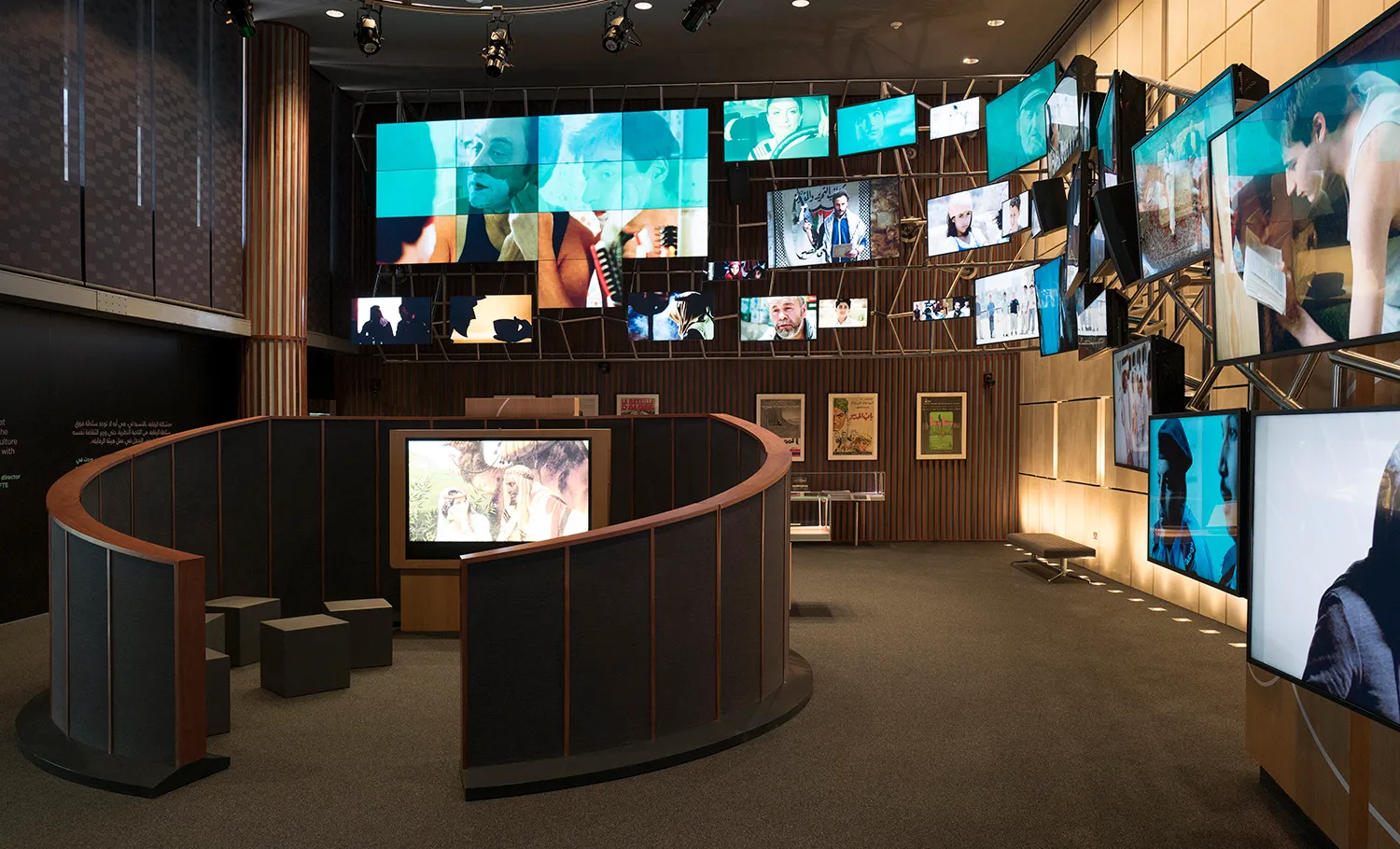 Digital screens line the exhibition hall walls, with a seating area in the center.