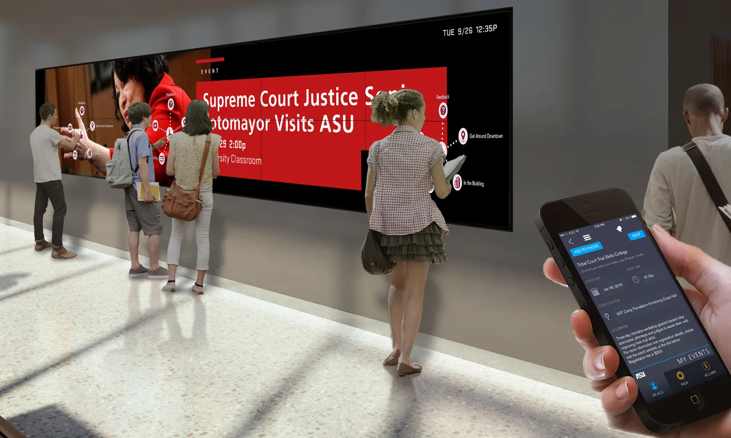 Students utilize the large media screen showing campus information. Hand on foreground depicts usage of the mobile app.