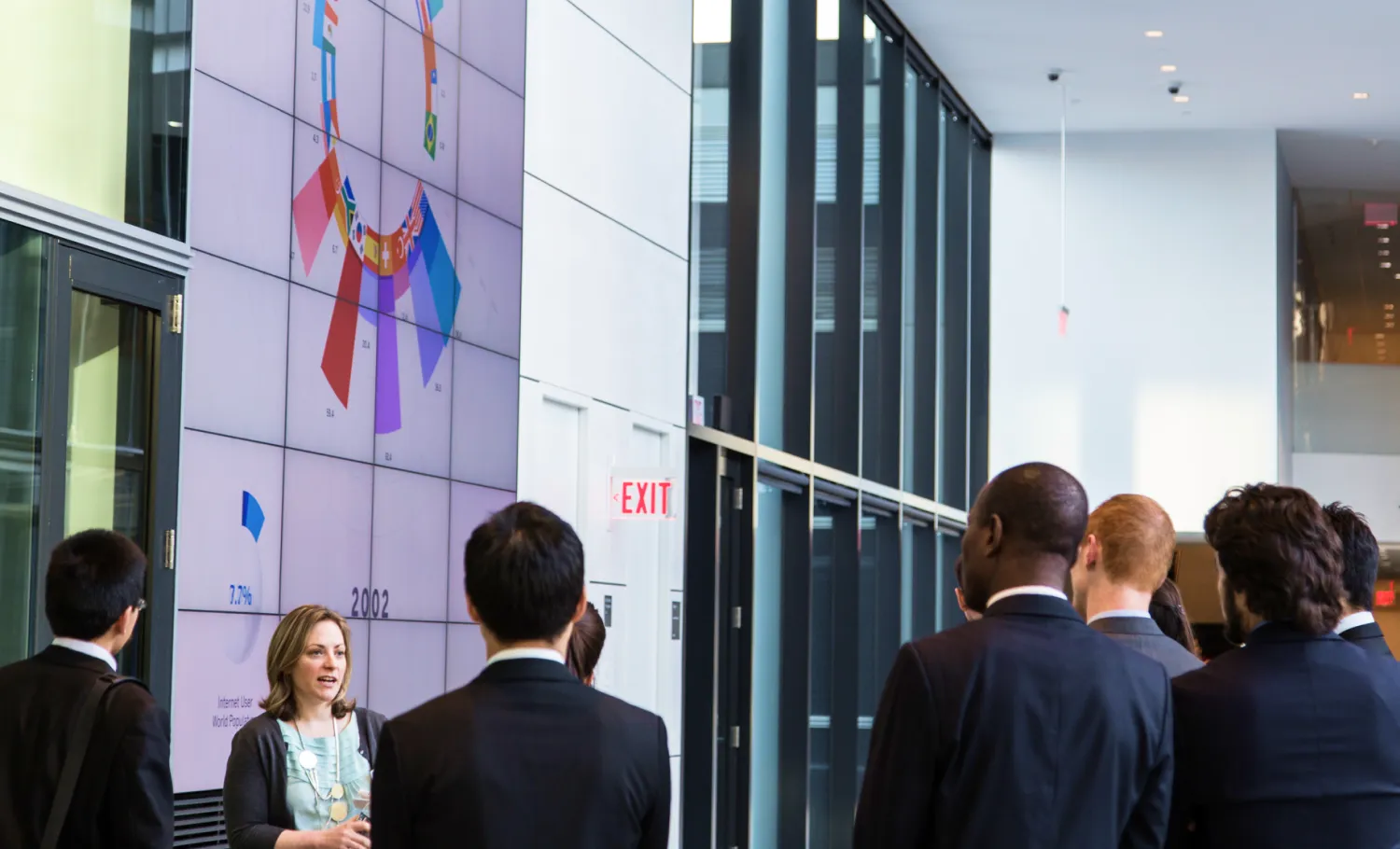 A group of businesspeople standing in front of large digital information screen.