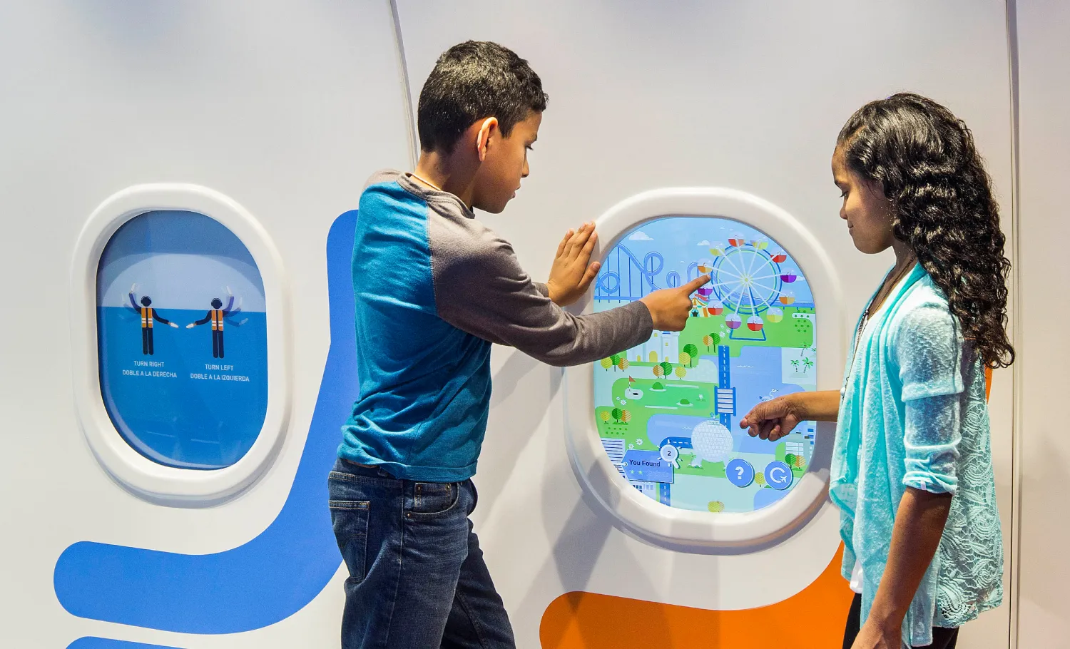 Children playing with an interactive screen shaped like an airplane window.