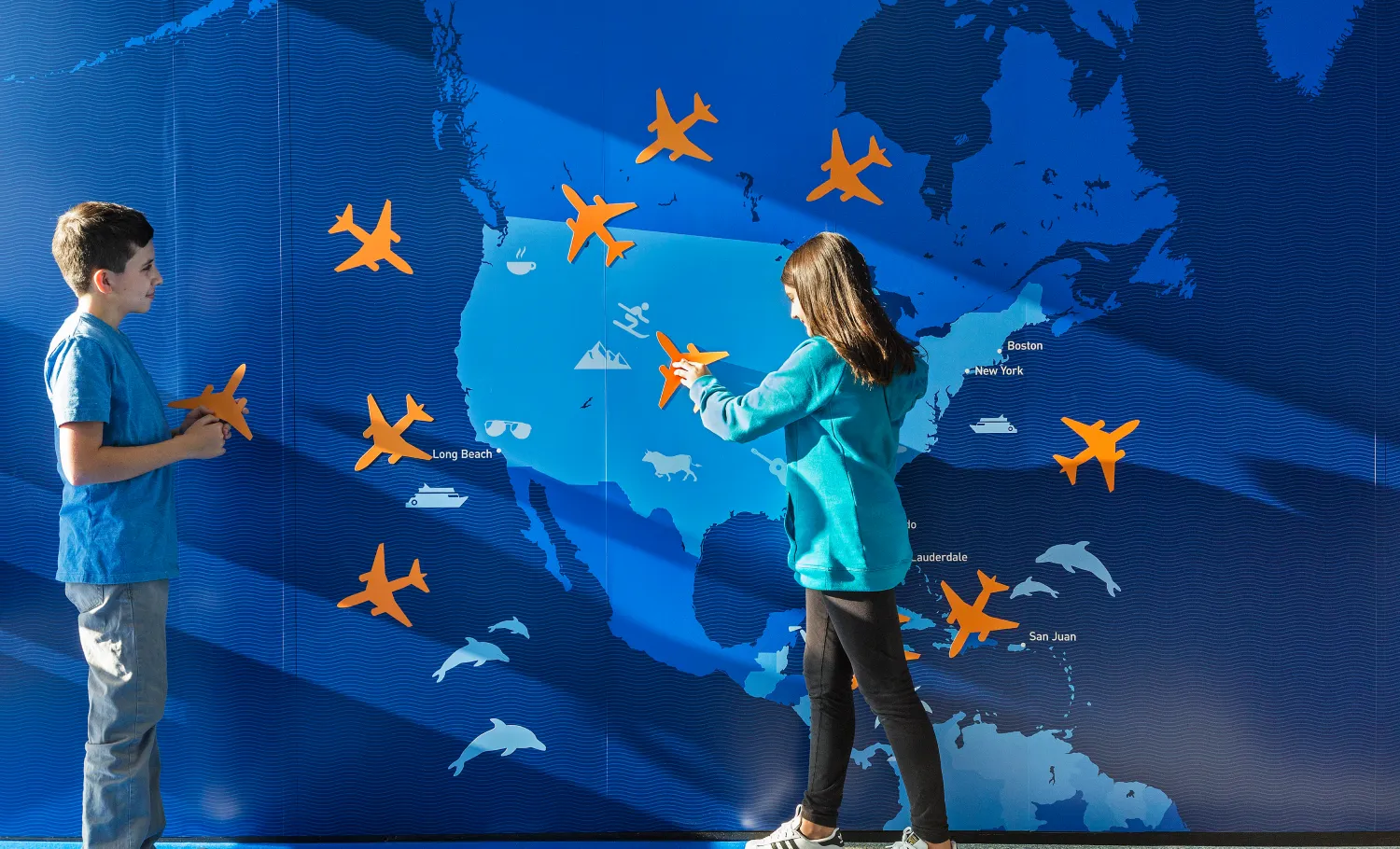 Children putting up airplane-shaped stickers onto a graphic wall panel depicting United States .