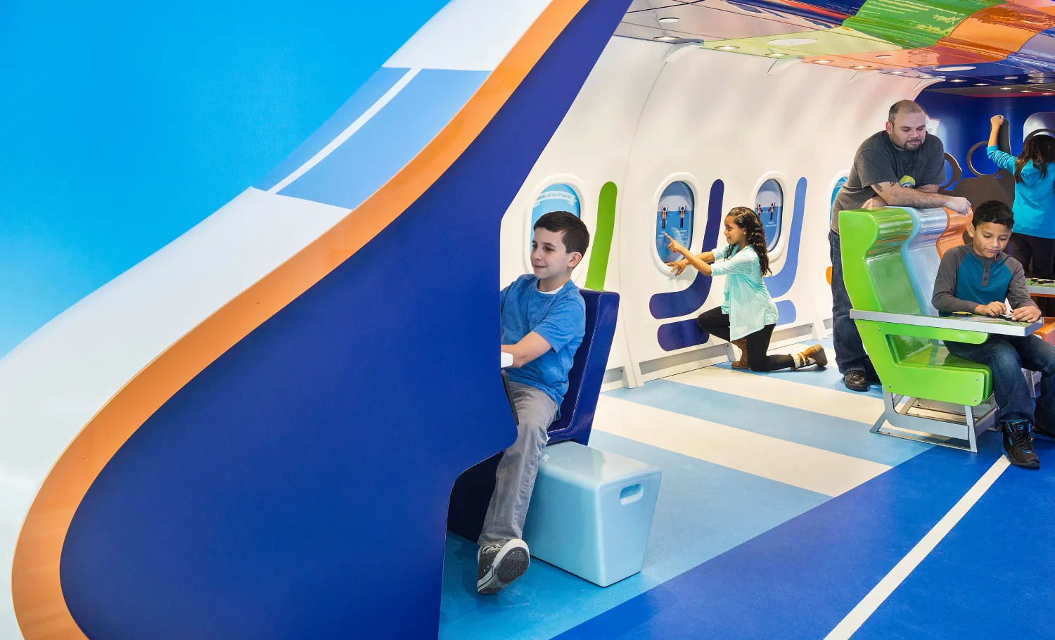 Children playing with various interactives in the PlaySpace modelled to resemble the interiors of an airplane.