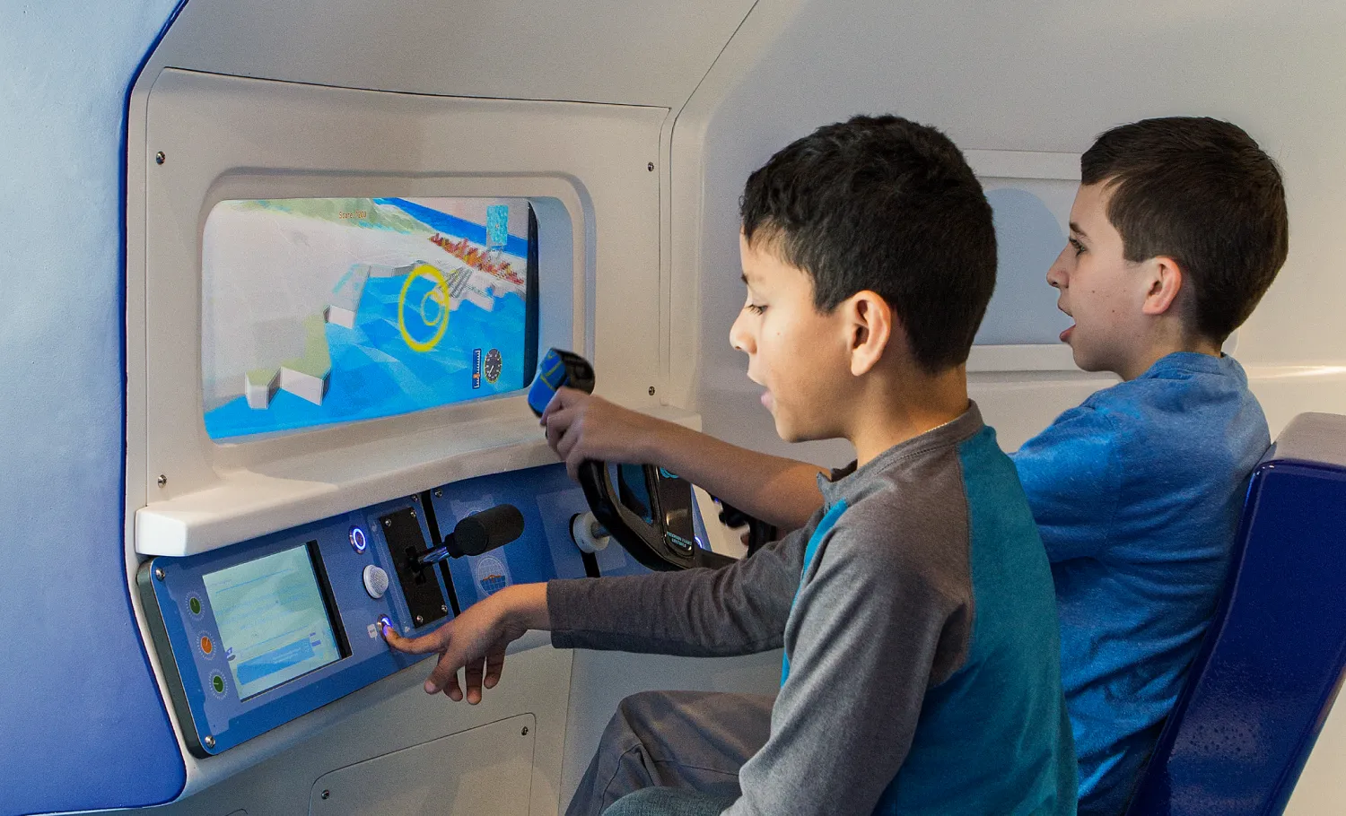 Seated children playing with a flight simulator modelled to look like simplified cockpits.