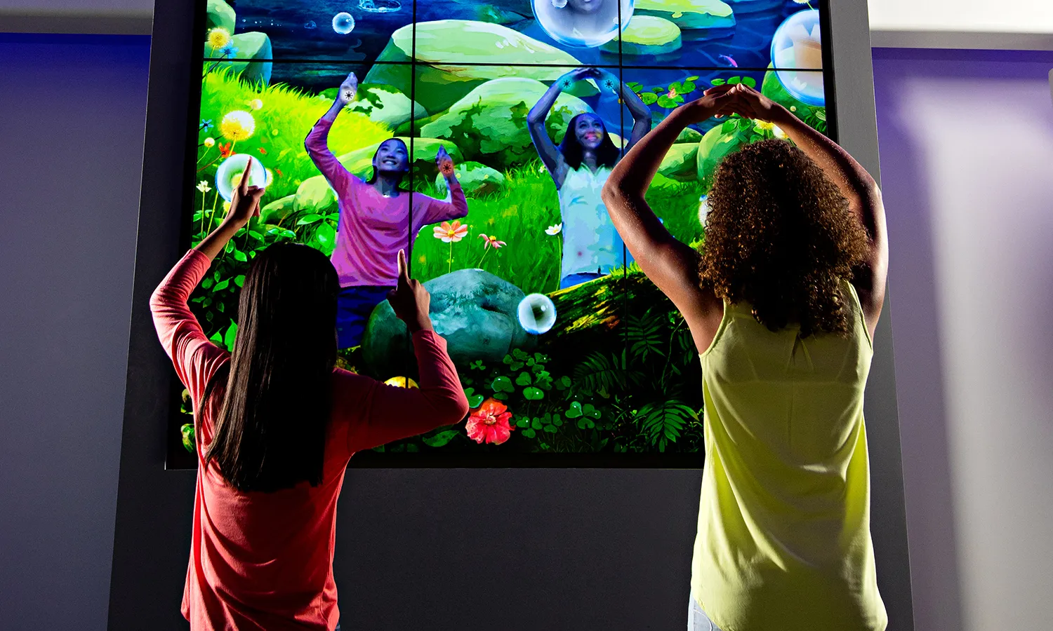 Children playing a motion-based game in front of a large vertical digital screen.