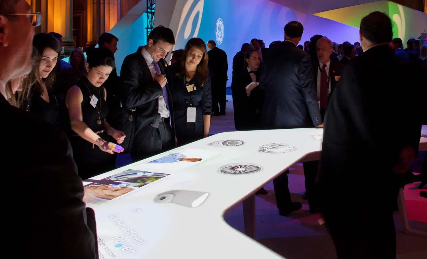 Crowd of visitors look at the digital table displaying GE's contribution to energy production.