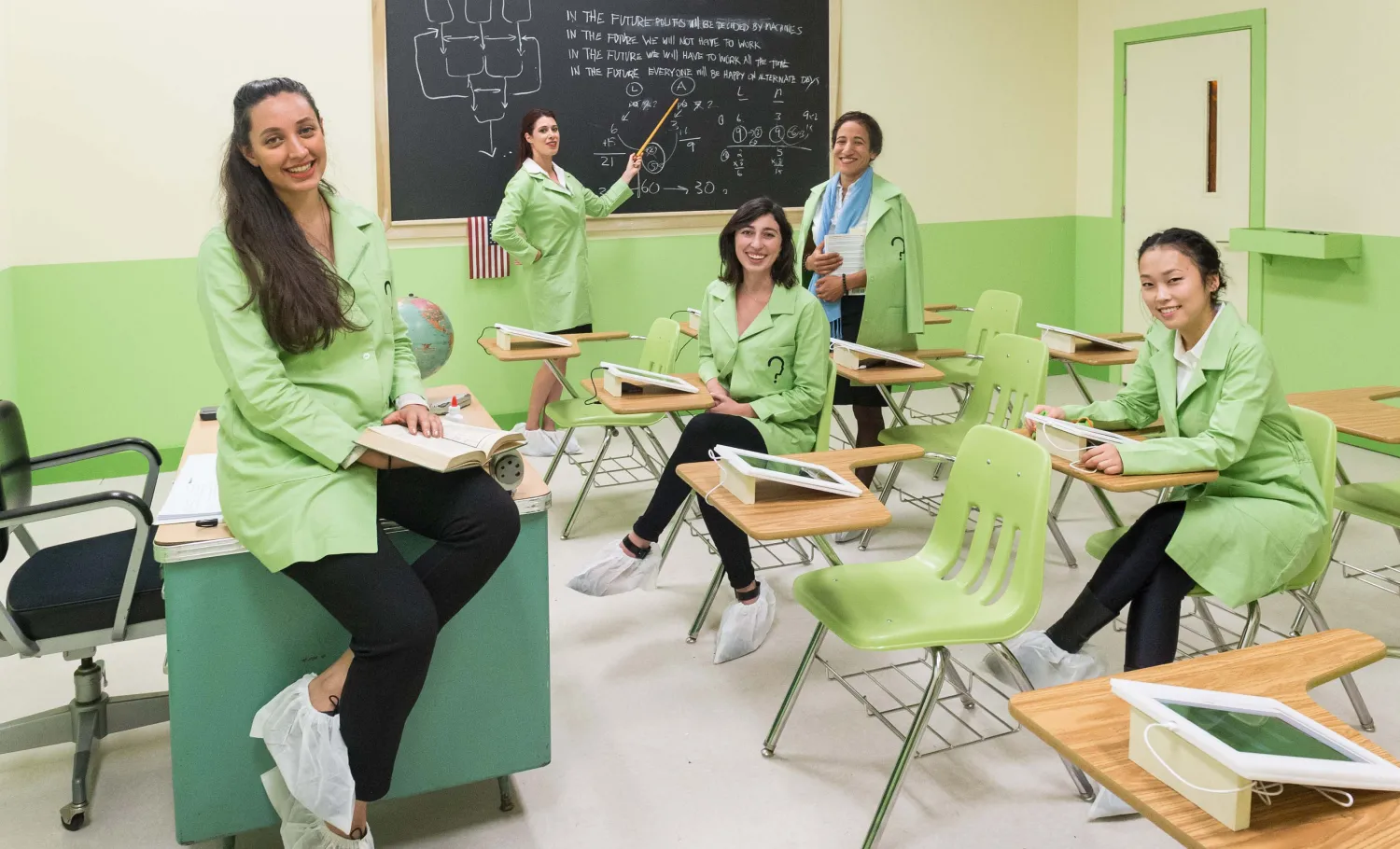 Group of women wearing green lab coats in a science classroom posing for the camera.