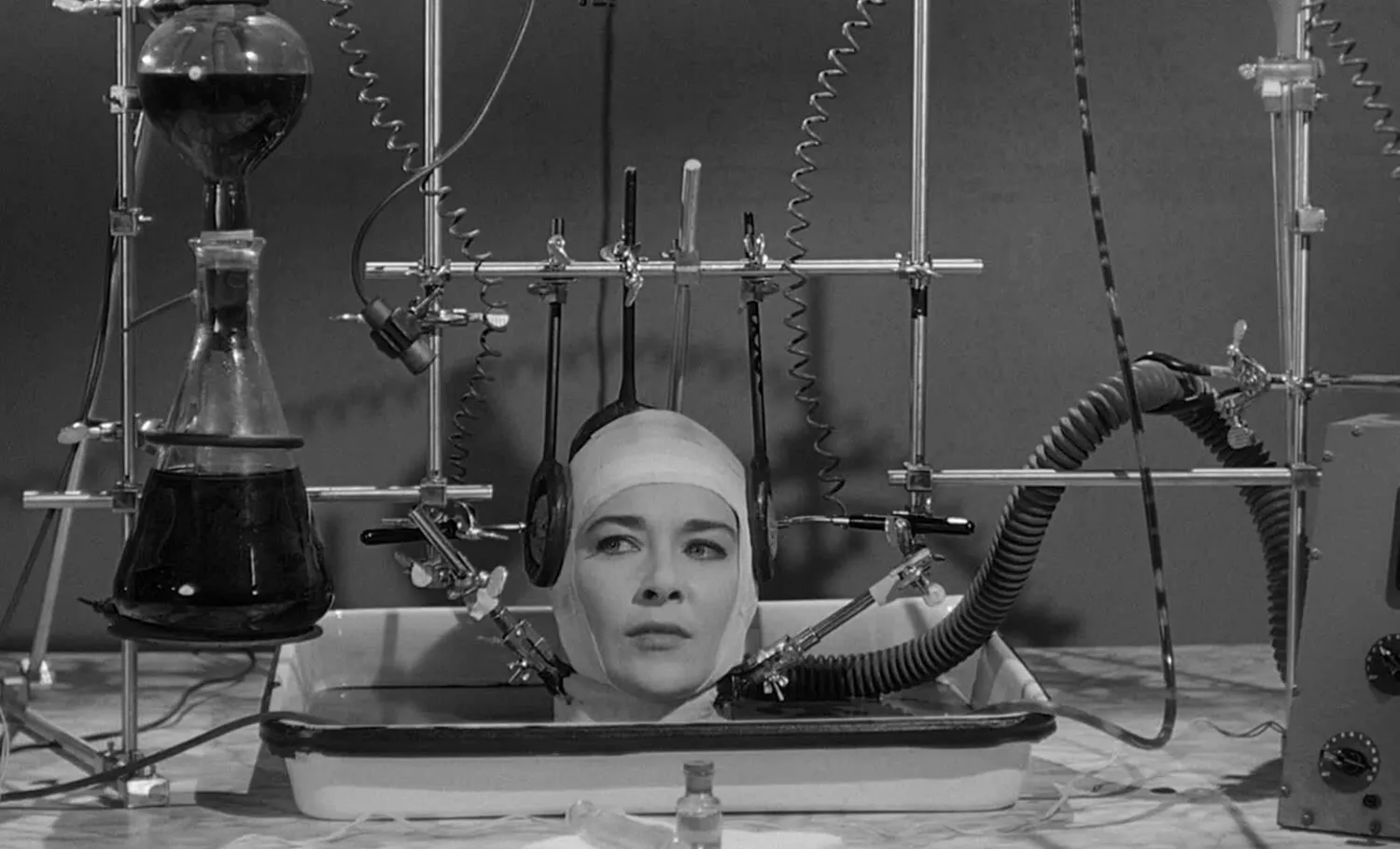 Black and white photo of a woman's on a lab table with lab equipments strapped to her head.