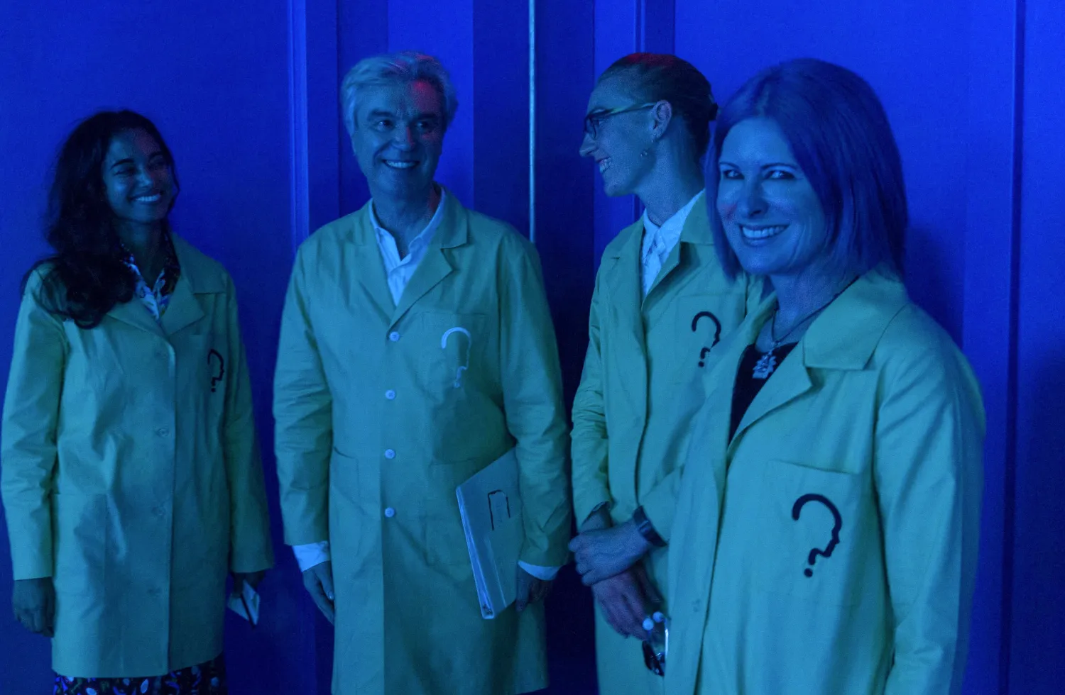Group of people wearing green lab coats smiling with each other.
