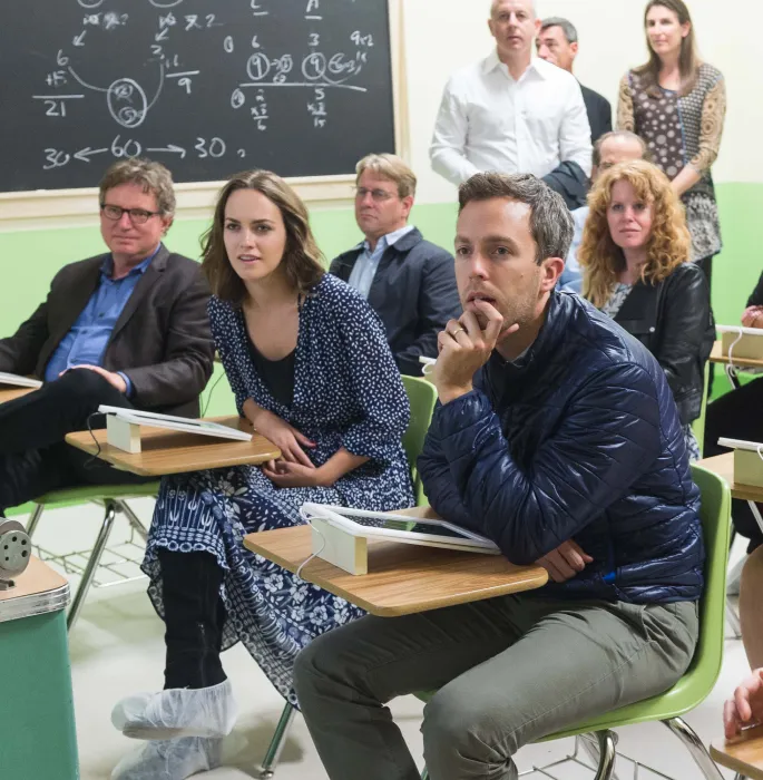 Group of people seated in a classroom listening intently to someone offscreen.