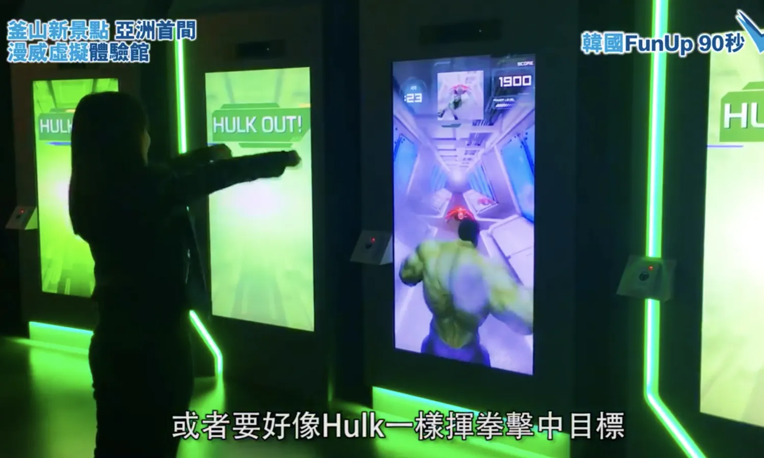A woman plays with a motion-based interactive game while The Incredible Hulk is displayed on a digital screen.