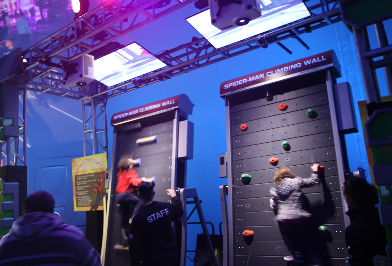 Two children climbing a rotating climbing wall. The title above the wall reads: "Spider-Man Climbing Wall"
