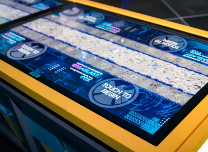Standby screen of a digital interactive. On-screen text reads: "Touch to Begin".