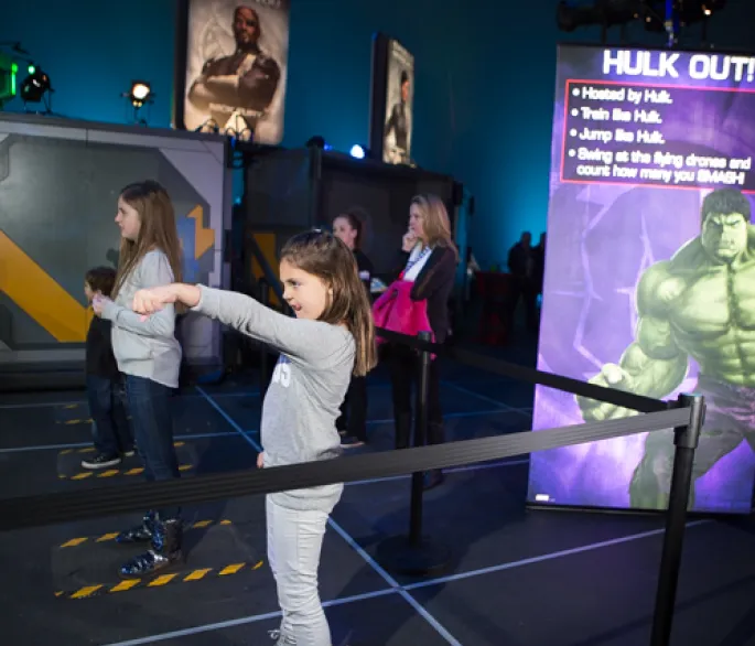 Children stand in front of an interactive screen while their guardians watch from behind.