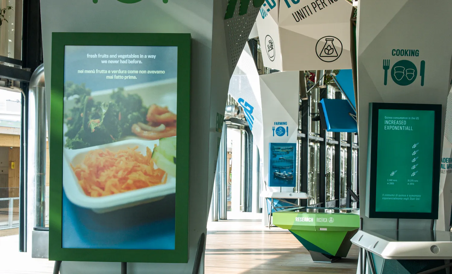 Empty exhibition hall with a number of digital kiosk screens showing food related infographics in both English and Italian.