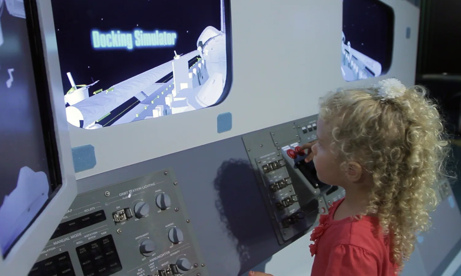 A young girl interacting with a space flight simulator game. Onscreen text reads "Docking Simulator".