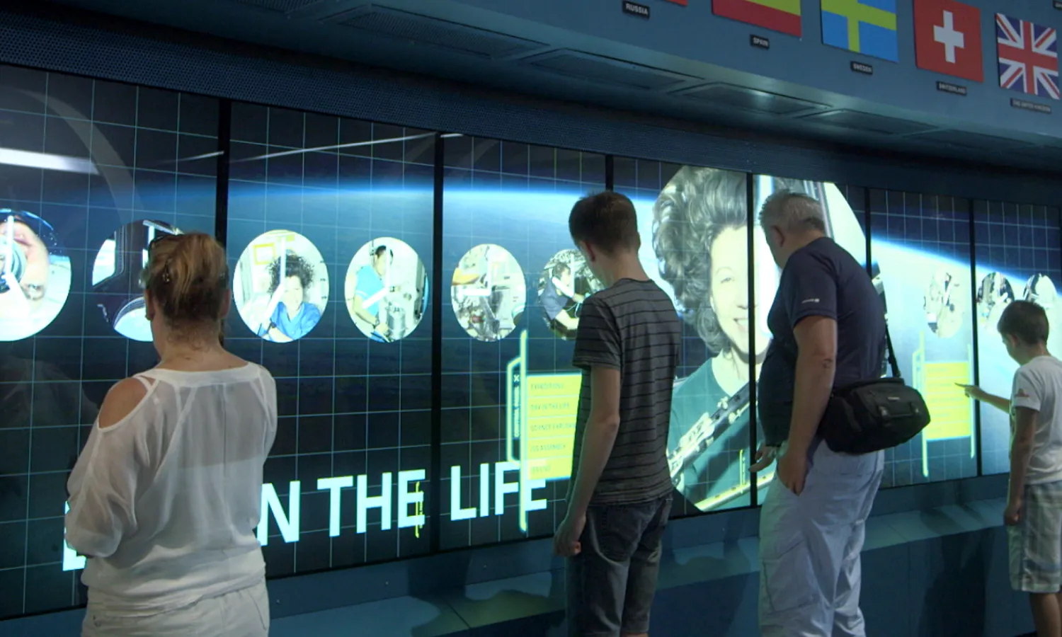 Visitors stand in front glass display cases with interactive screens to read about different artifacts.