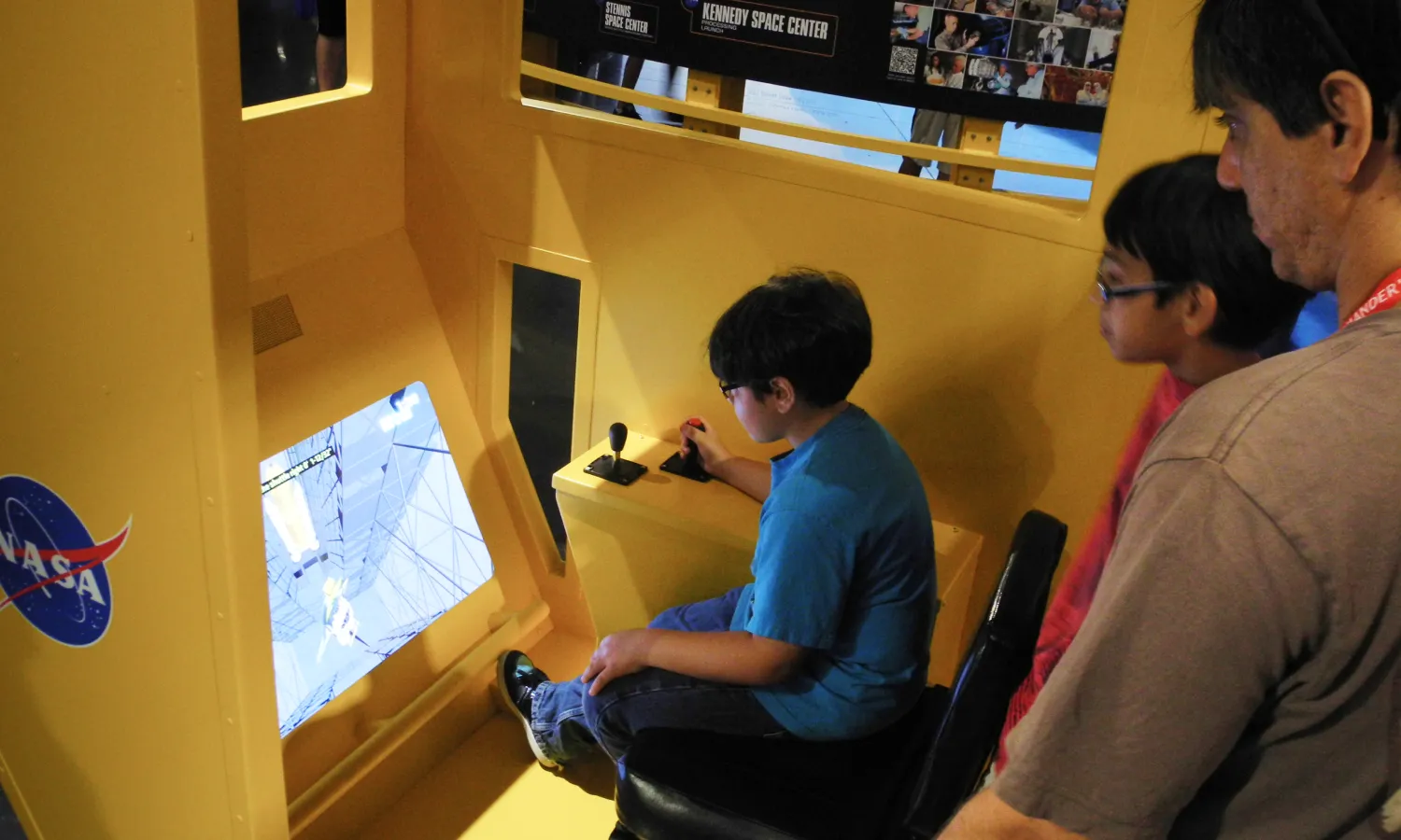 A child plays on an interactive kiosk as an adult looks on behind.
