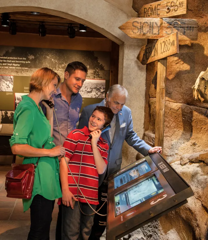 A family uses a telephone connected to a digital touchscreen kiosk to listen to stories and videos of WWII soldiers.