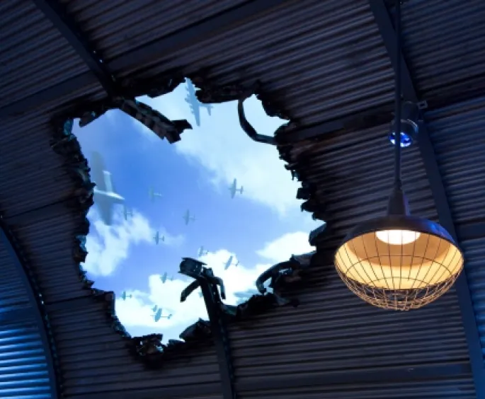 Exhibition hall ceiling showing blue skies, mimicking a hole created by an airbomb blast.