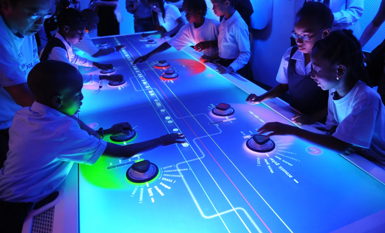 Groups of children interact with the digital Music Mixer interactive table.