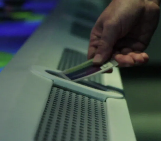 A hand holding an entrance card up to an entry gate card reader.