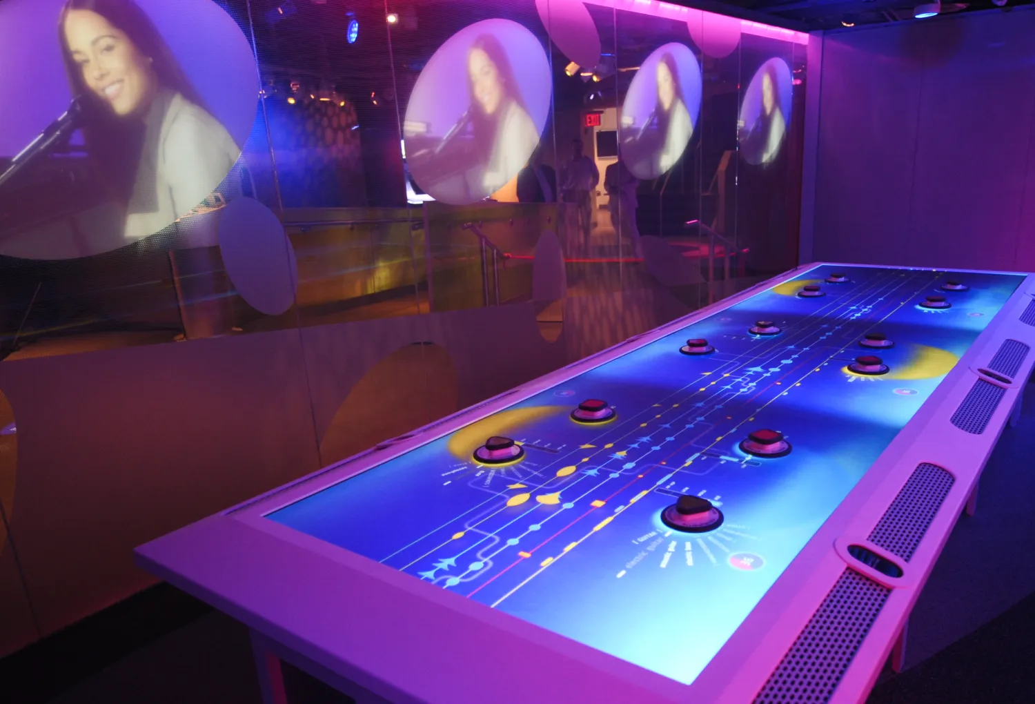 Full view of the Music Mixer interactive table and screens playing instructional videos above.